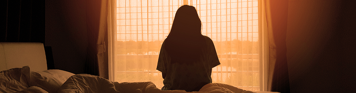 A person sat on a bed looking out of the window